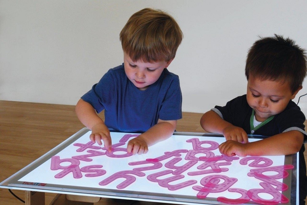 Zwei kleine Jungs legen transluzente Buchstaben auf Leuchttisch Zwei kleine Jungs legen transluzente Buchstaben auf Leuchttisch