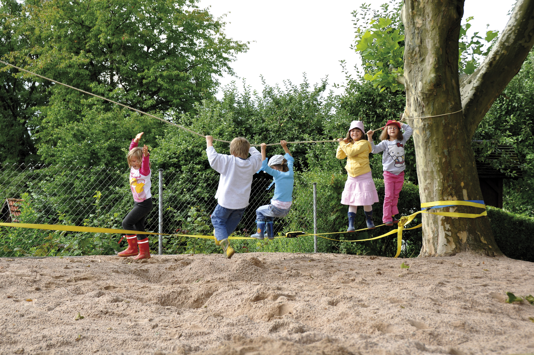 Kinder klettern an Slackline mit Halteseil