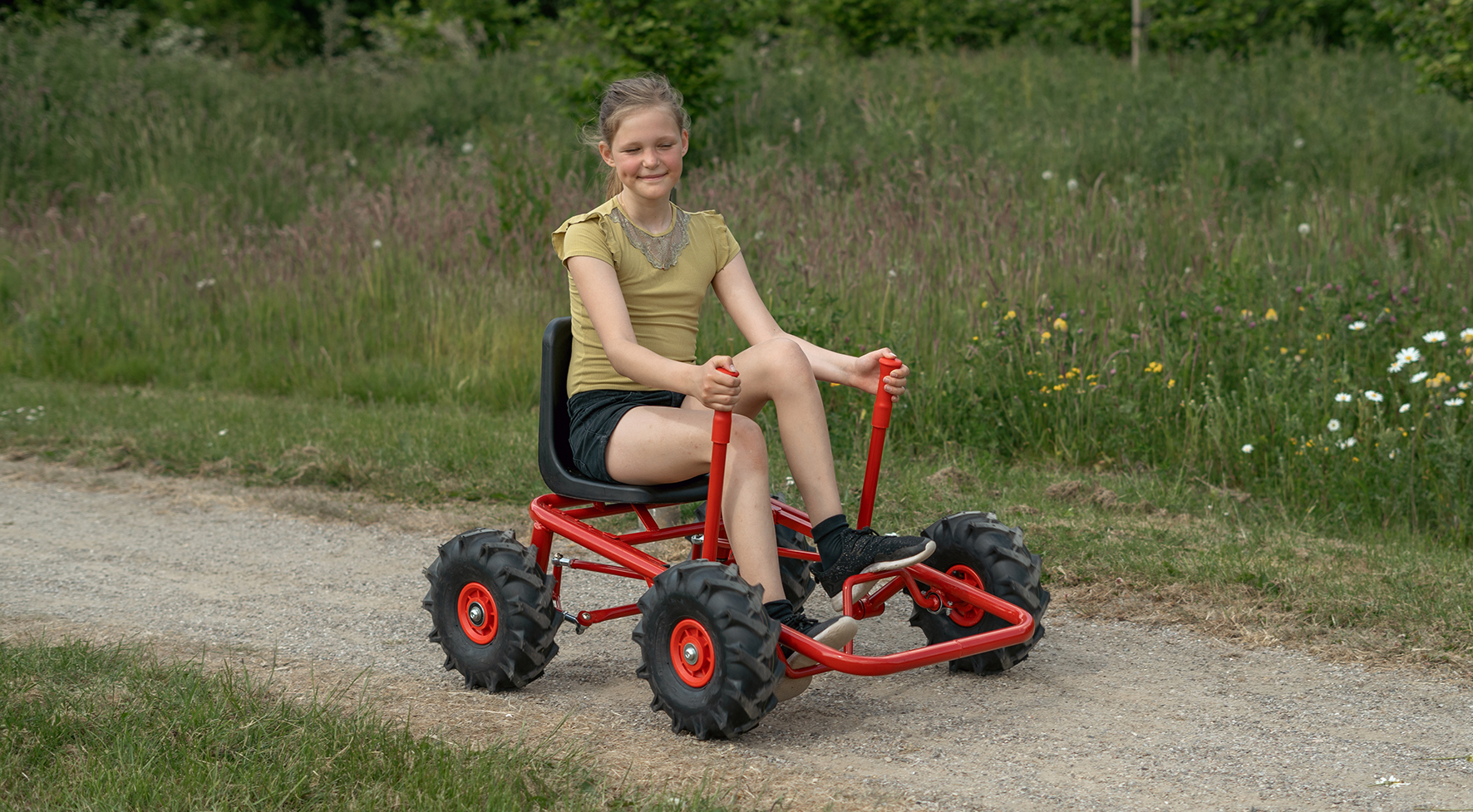 Großes Mädchen zieht kleinen Jungen auf ROSE Dreirad mit Anhänger Mädchen fährt ROSE Gokart